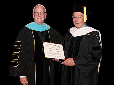 Jerry Scheidegger wearing black doctoral robes with white hood, being handed his honorary doctorate by 总统 Porter wearing black doctoral robes with blue hood.